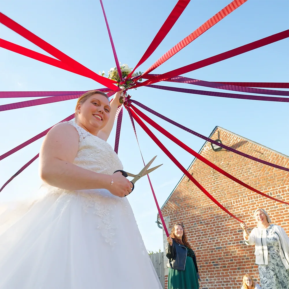 la mariée tient des ruban en l'air. De l'autre main, elle porte des ciseaux. C'est le jeu de ruban lors de son mariage.