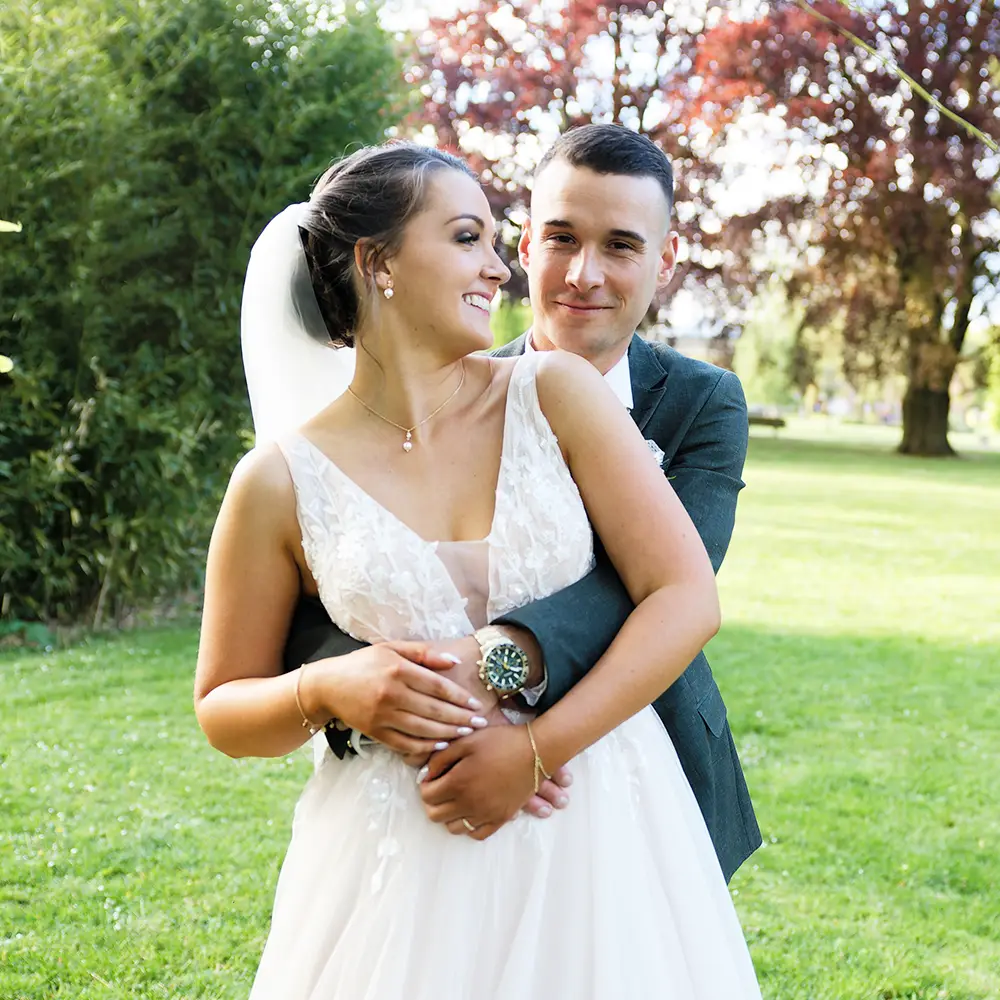 Jeunes mariés posant dans le parc de Lievin, pour la séance couple. Lui la prend par la taille, elle devant, a la tête tournée pour le voir.