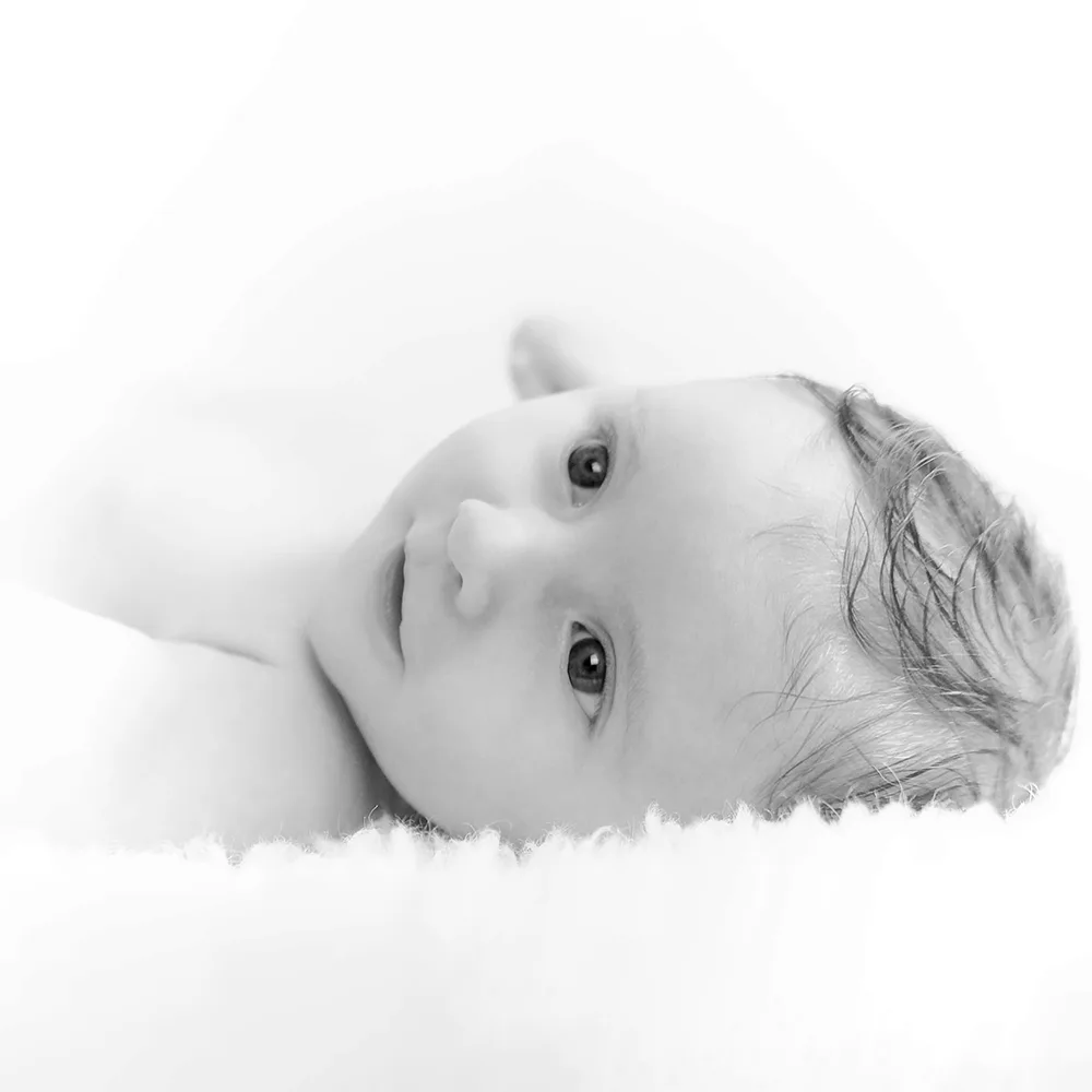 Shooting d'un bébé : la petite est allongée sur le dos. Photo en noir et blanc, en high key.