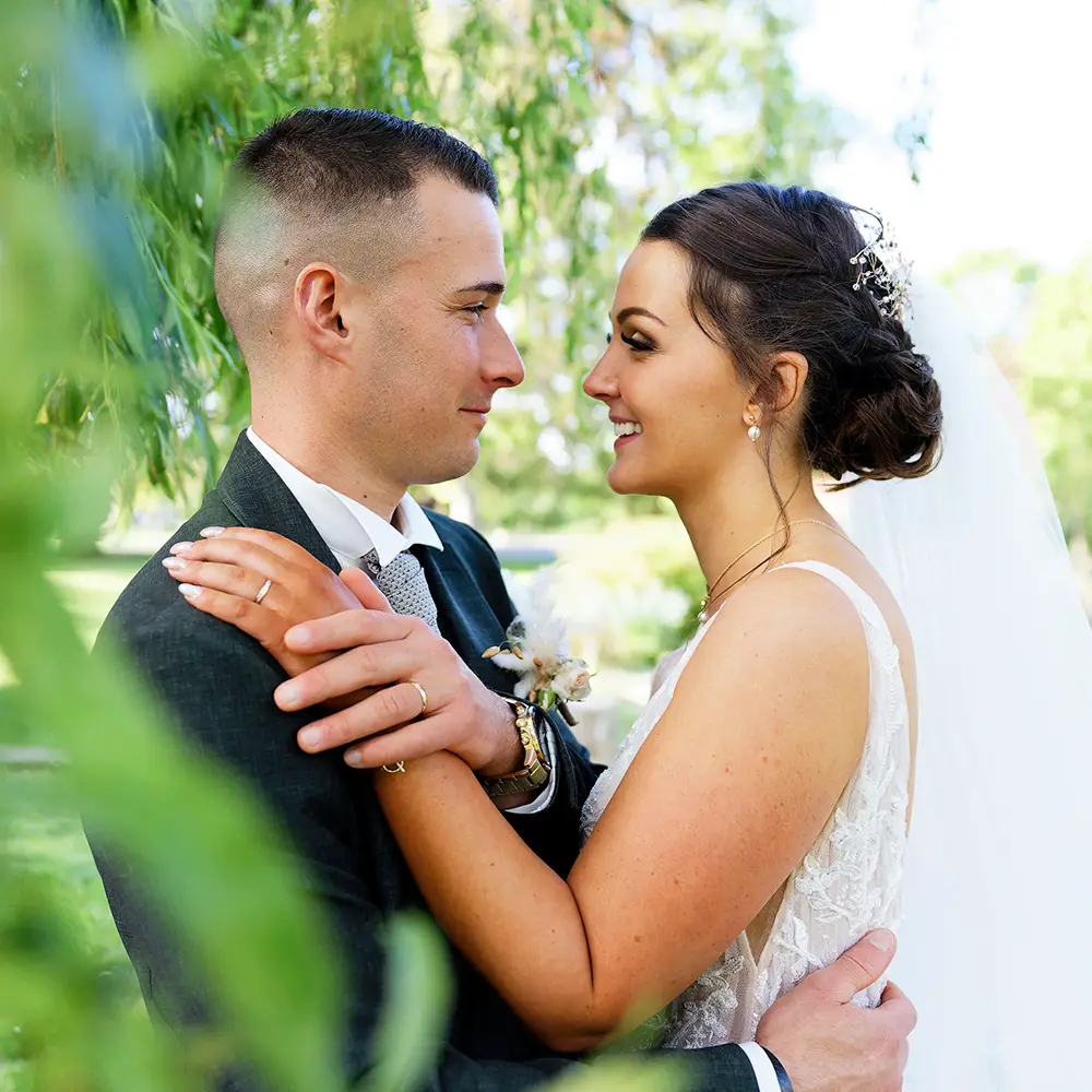 Portrait de couple de mariés dans un jardin | Photographe Arras Photographie de couple de jeunes mariés, tendrement enlacés et se regardant avec amour dans un jardin public à Liévin. Un instant romantique capturé par un photographe de mariage dans les Hauts-de-France.