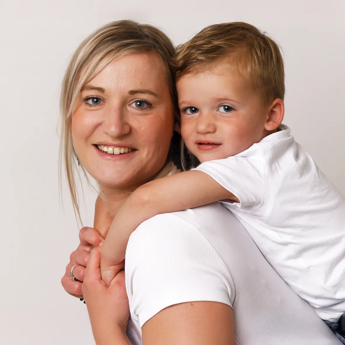 Gros plan d'une mère souriante portant son jeune fils sur son dos, un portrait de maternité et d'amour familial pris par un photographe de Sainte-Catherine.
