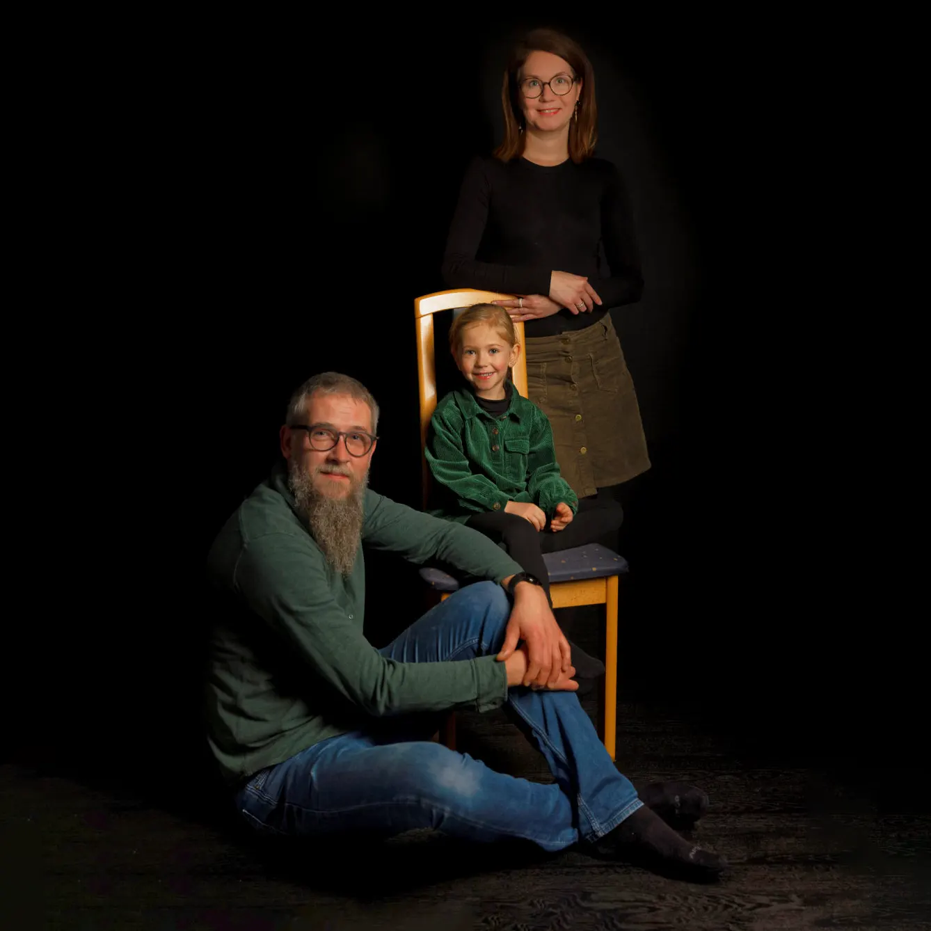 Portrait de profil d'une famille de trois personnes sur fond sombre, avec un éclairage de studio dramatique mettant en valeur les silhouettes, par un photographe de portrait à Sainte-Catherine.