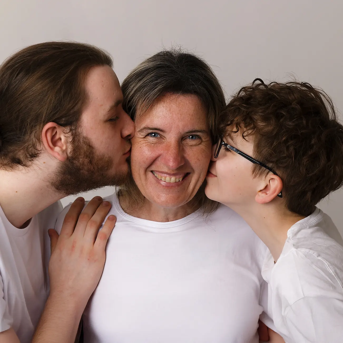 Gros plan d'une mère souriante au centre, recevant des baisers de ses deux fils sur les joues, une photo de portrait de famille affectueuse prise à Sainte-Catherine.