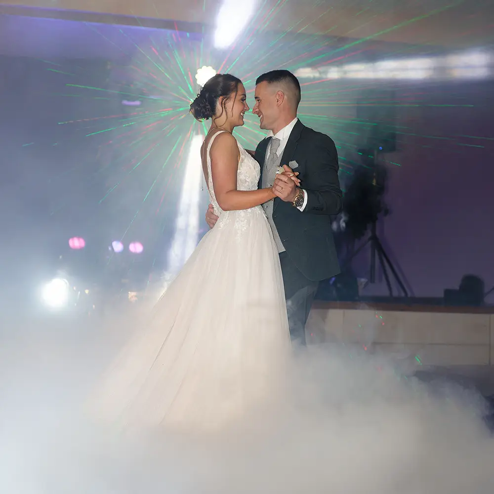 Première danse des mariés à Souchez | Photographe Mariage Lens Photographie de la première danse de Manon et Vincent, les jeunes mariés, sur la piste de danse. Des lumières colorées et de la fumée créent une ambiance magique. Photographe de mariage à Souchez, près de Lens.