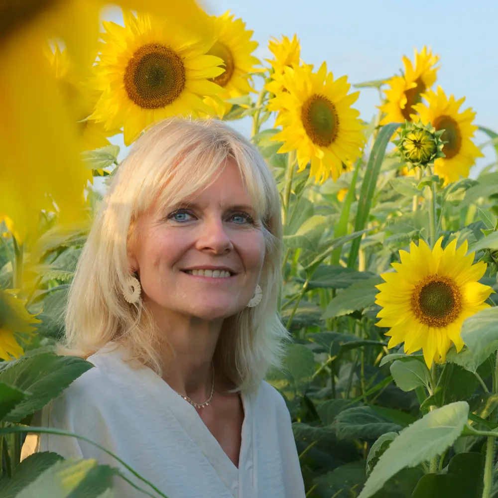 Portrait de femme souriante au milieu de grands tournesols, photo en extérieur à Arras et Sainte-Catherine.