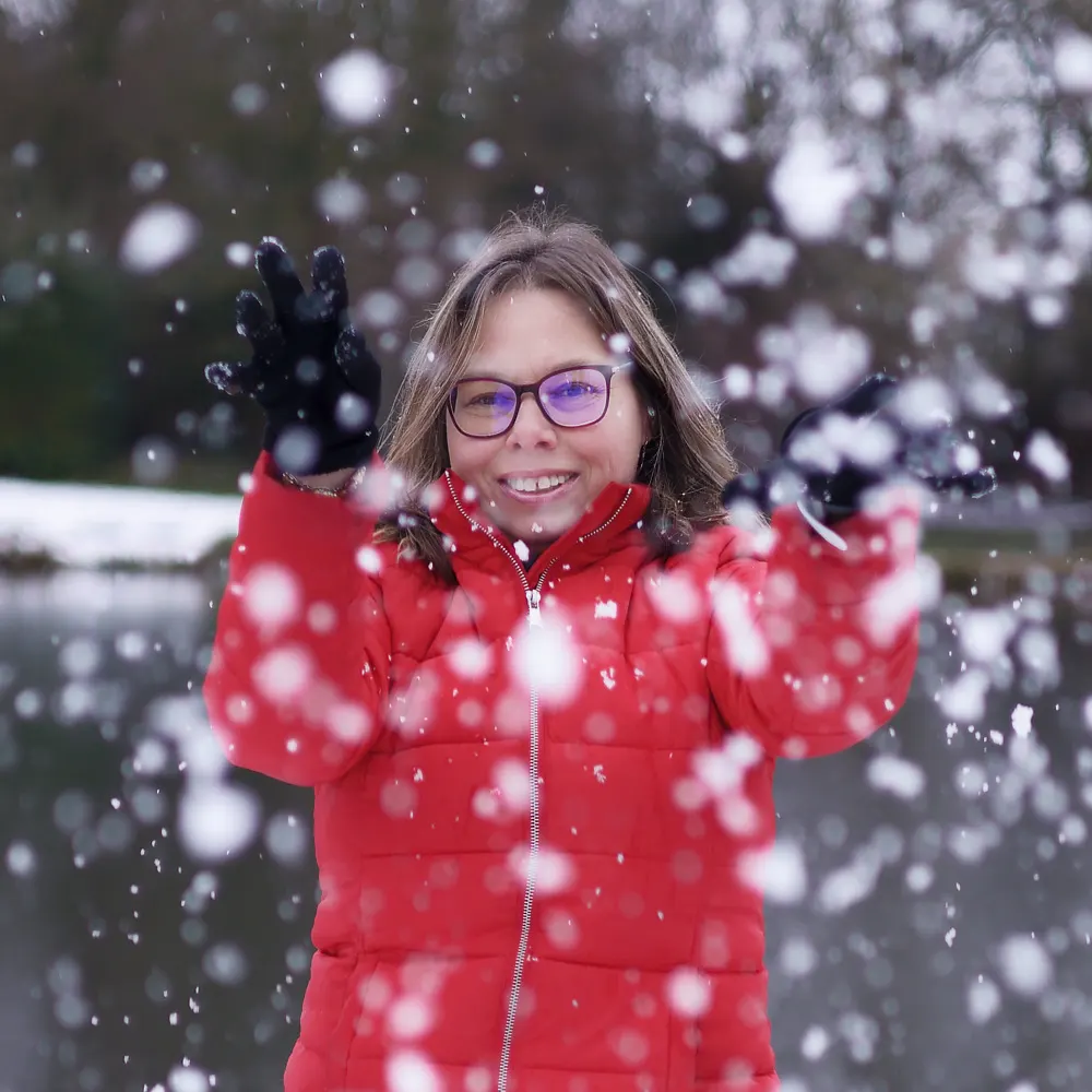 Portrait de femme lançant de la neige en riant, séance photo d'hiver pleine de joie et de mouvement près d'Arras.