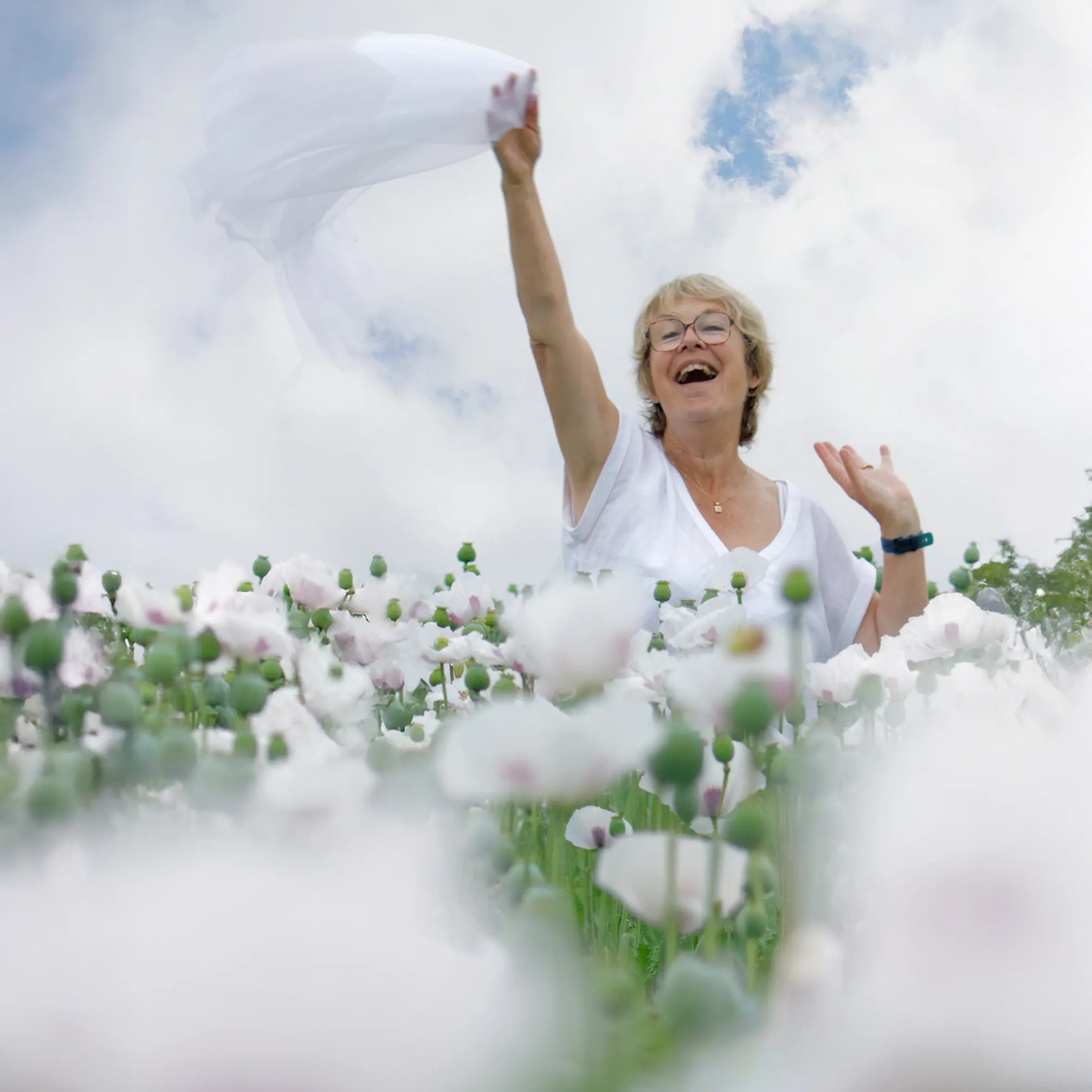 Portrait de femme riant et agitant un foulard dans un champ de pavots blancs, photo en extérieur à Sainte-Catherine près d'Arras.