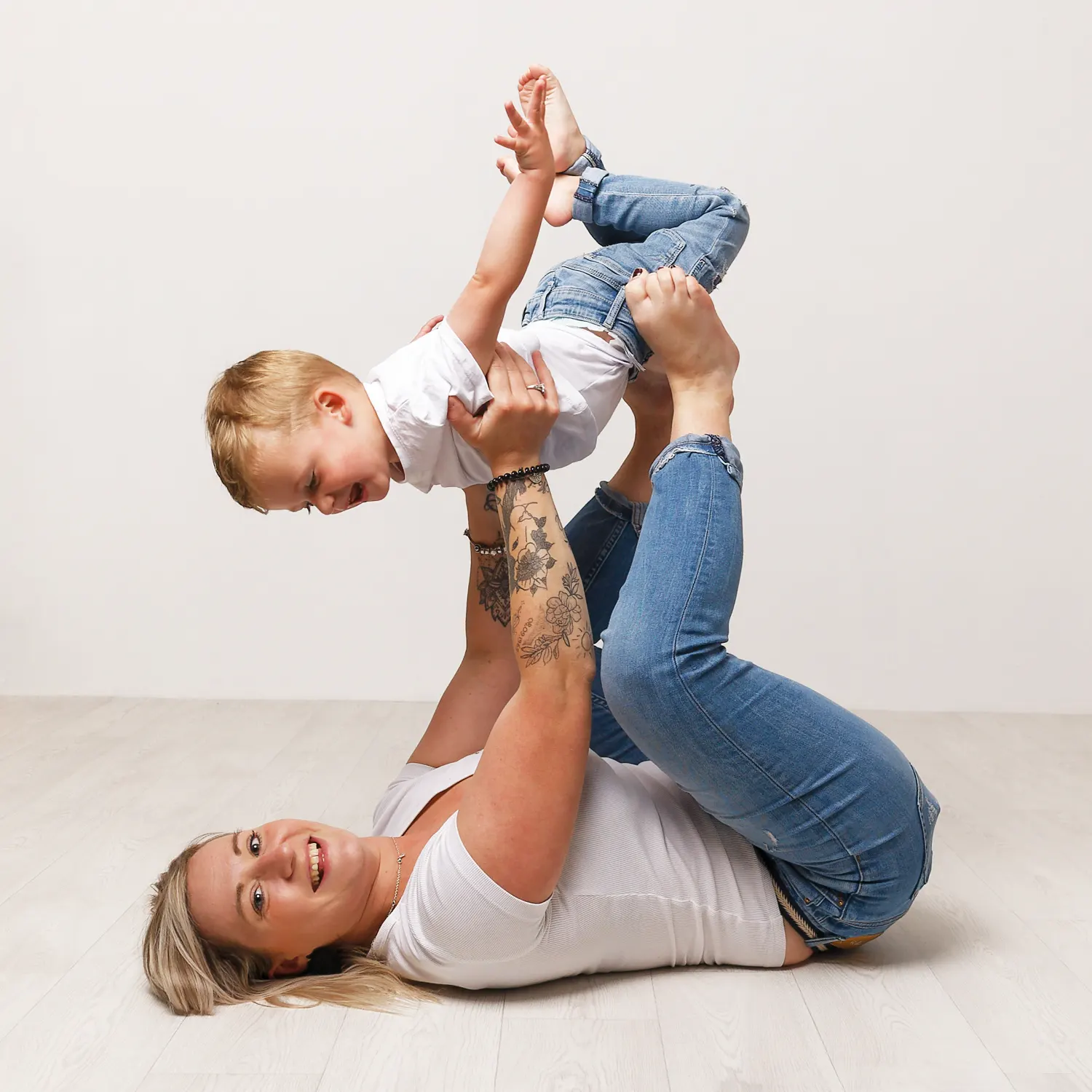 Photo mère enfant, pleine de jeu et de rires, montrant une mère allongée sur le dos tenant son fils en l'air avec ses pieds, un moment de joie capturé par un photographe à Sainte-Catherine