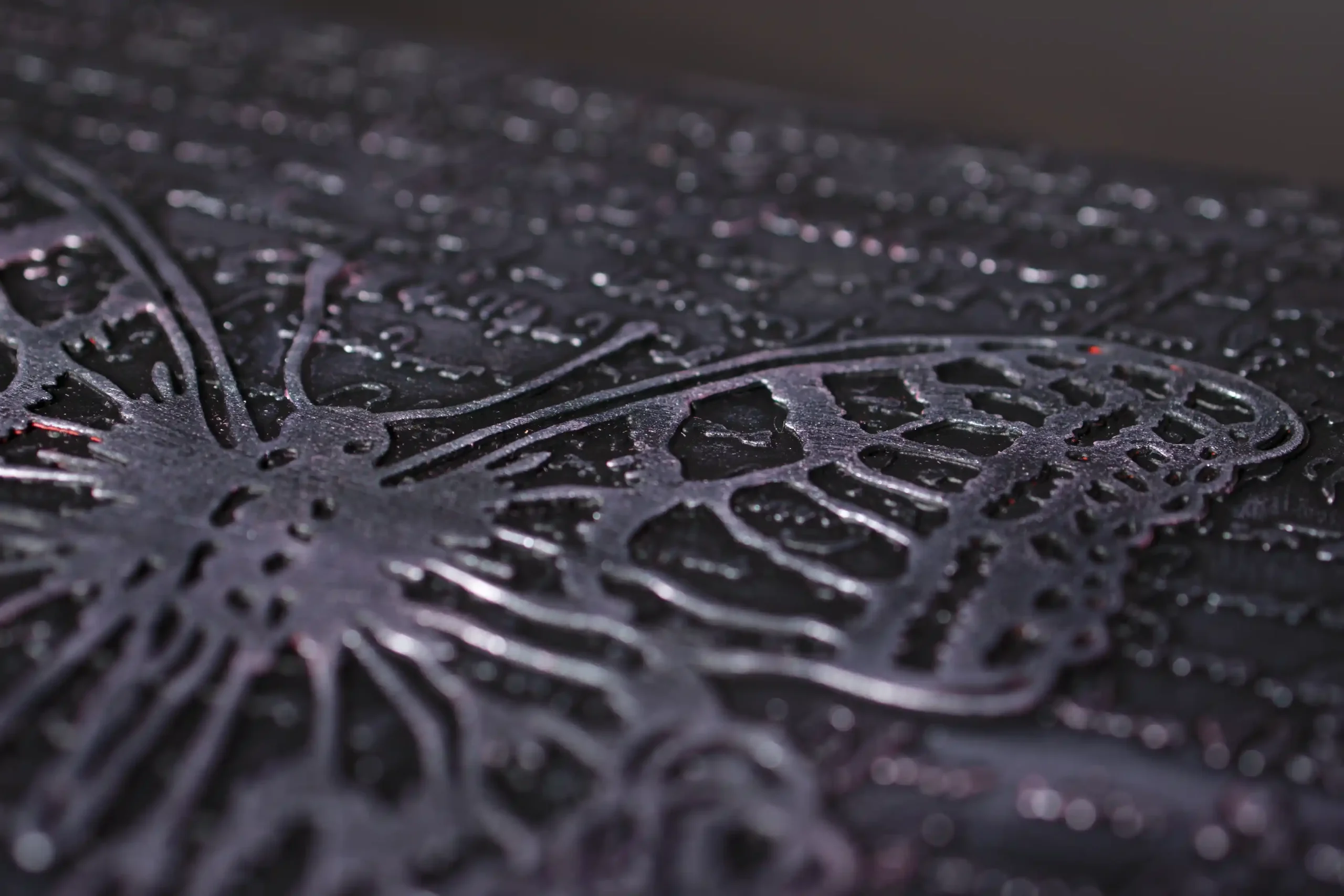 Gros plan en macro sur la couverture d'un album photo noir et texturé. Un motif de papillon en métal est posé en relief, sur un fond de texte ou d'écriture sculpté, soulignant la texture craquelée de la couverture.