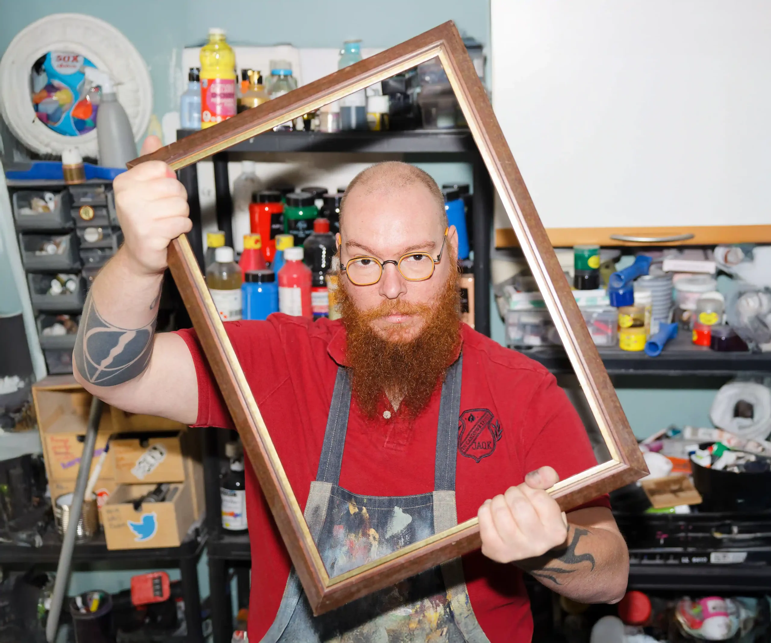 Un artiste barbu tient un cadre vide devant lui dans son atelier, invitant à découvrir l'art de la peinture.