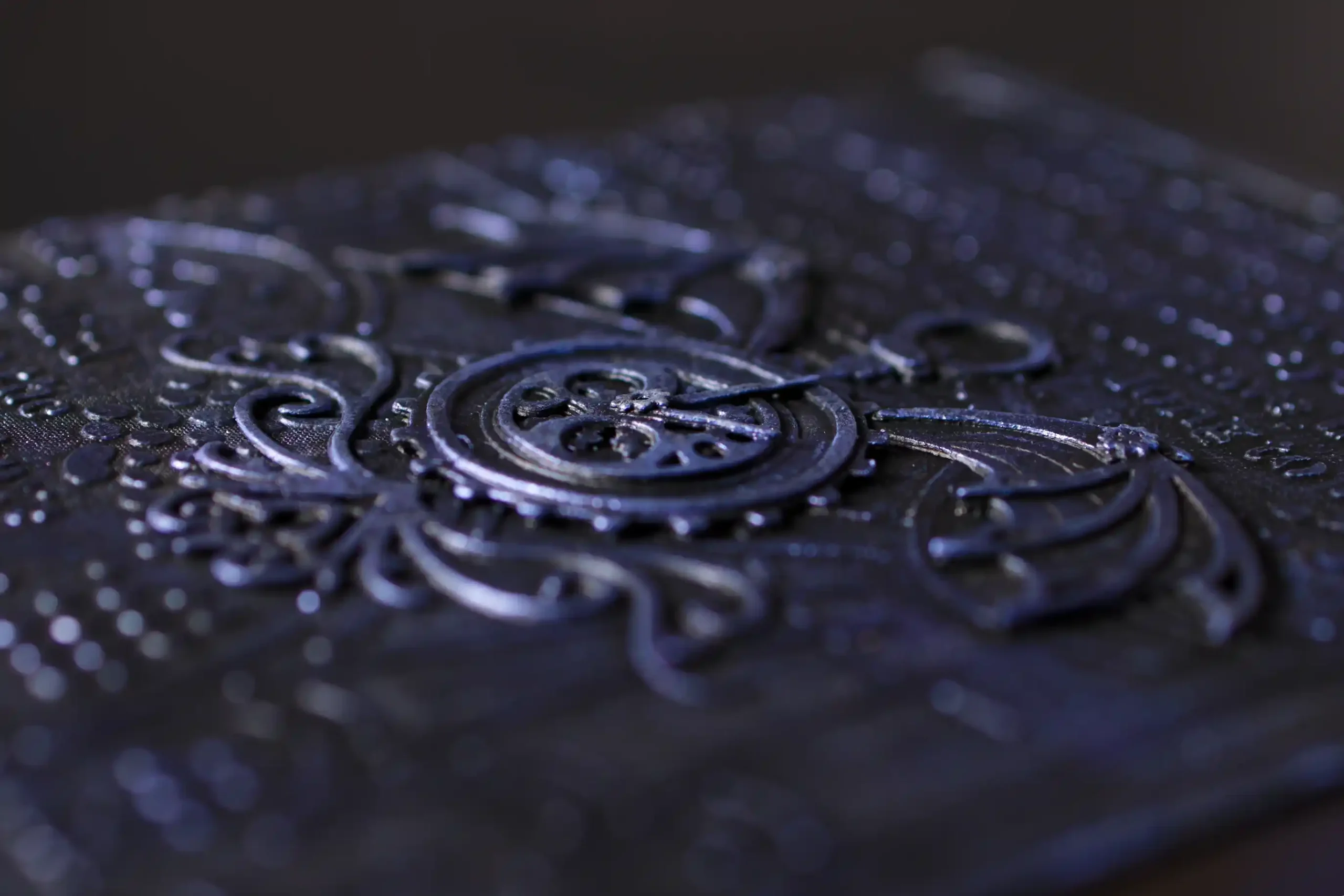 Gros plan en macro sur la couverture d'un carnet texturé, dans des tons violets et sombres. Le relief montre des motifs décoratifs et un engrenage central de style Steampunk, soulignant la texture granuleuse de la matière.