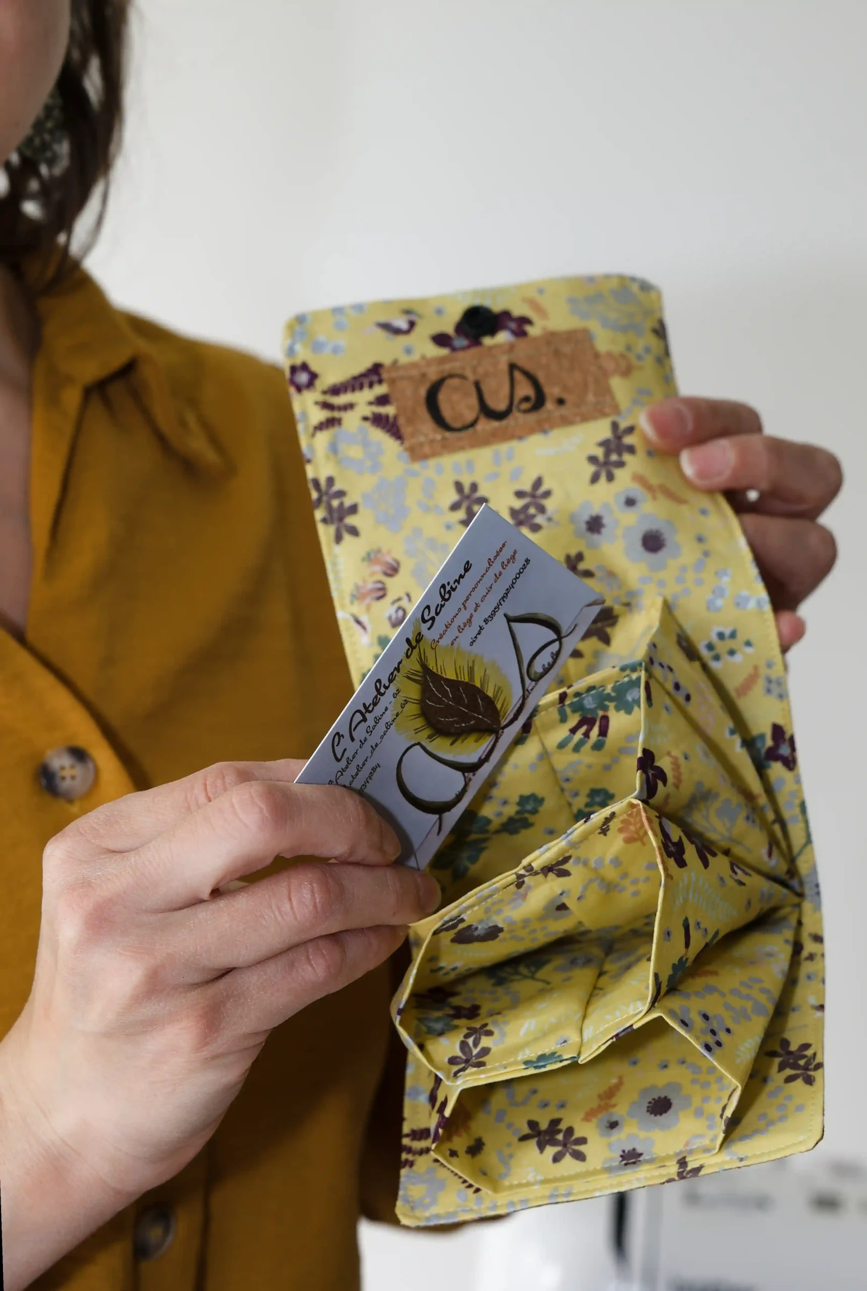 Une couturière tient un porte cartes en tissu qu’elle a cousu d'une main et sa carte de visite de l'autre, prête à échanger avec ses clients.