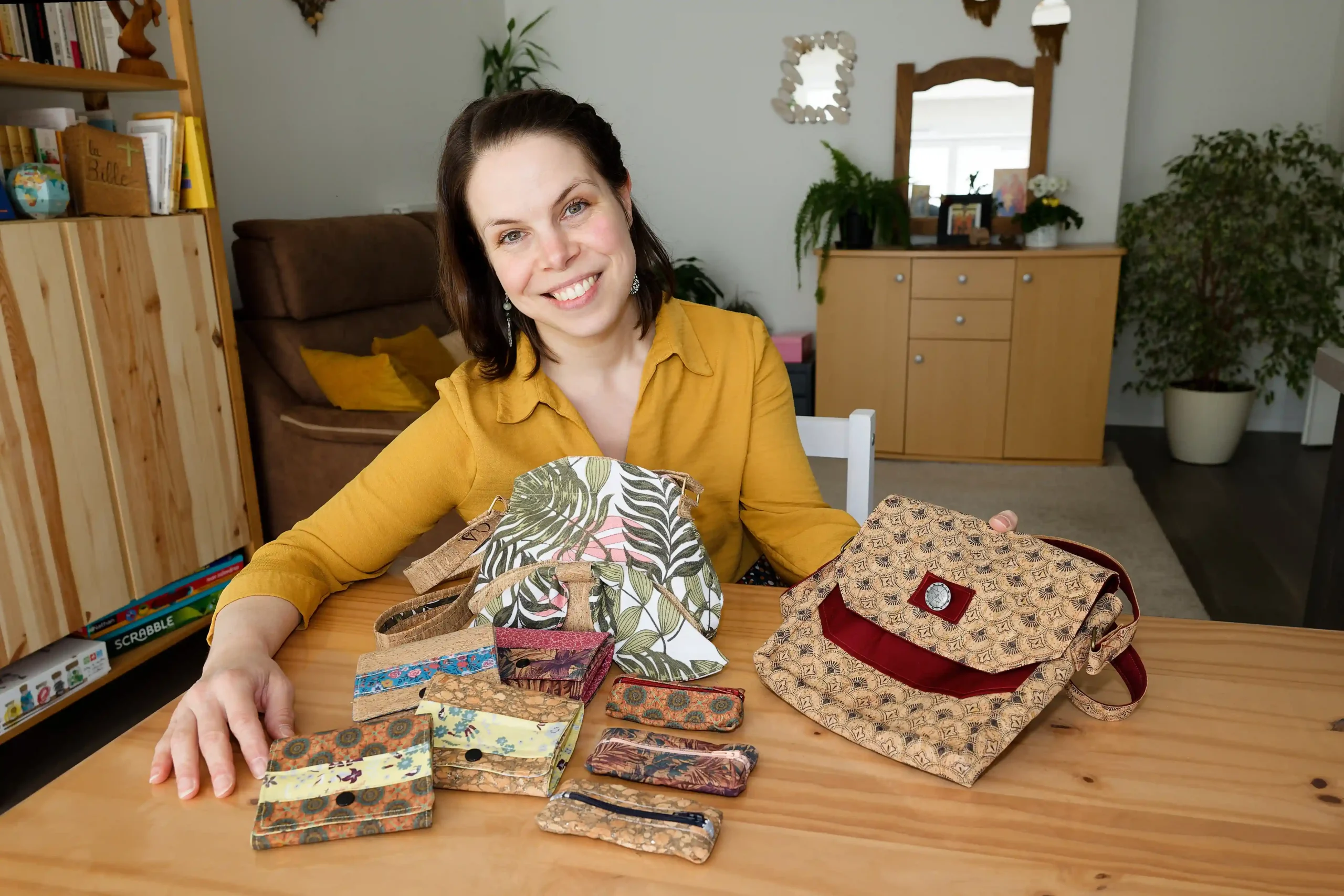 Une couturière souriante présentant une collection d'accessoires de mode, tels que des sacs, portefeuilles et pochettes.