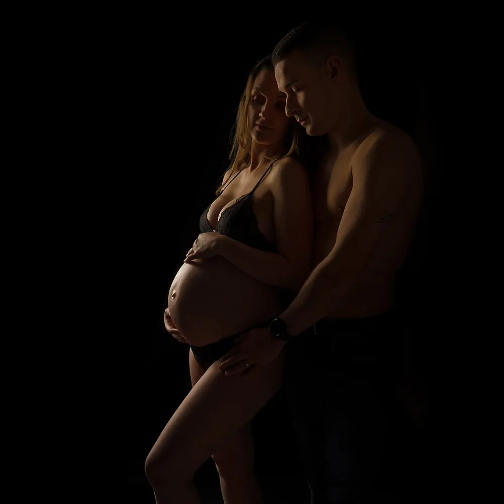 Photographie de grossesse sensuelle et artistique en studio, capturant un moment de complicité entre les futurs parents.<br />
