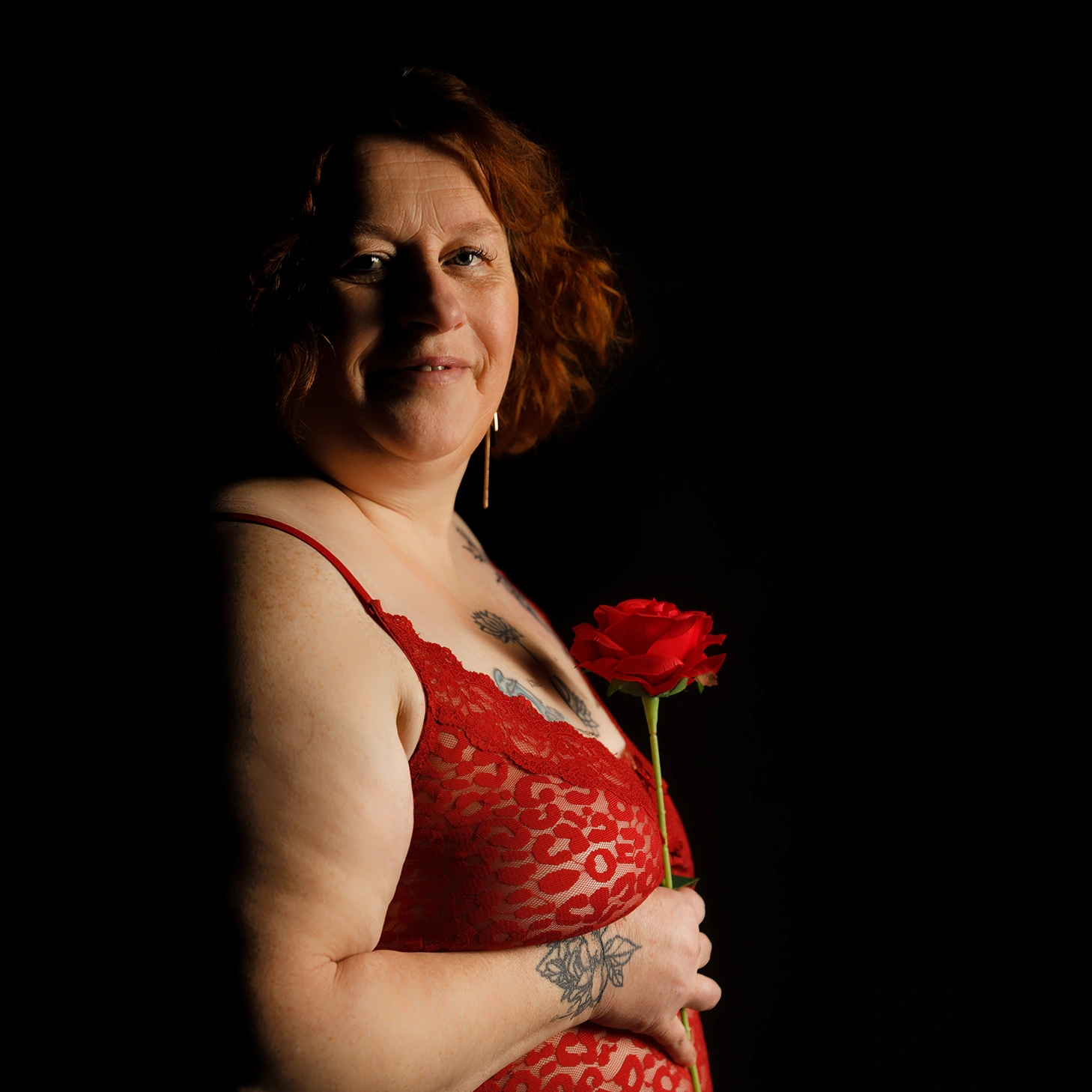 Gros plan d'une femme en lingerie rouge tenant une rose. Mise en lumière créative pour une séance photo boudoir près d'Arras.
