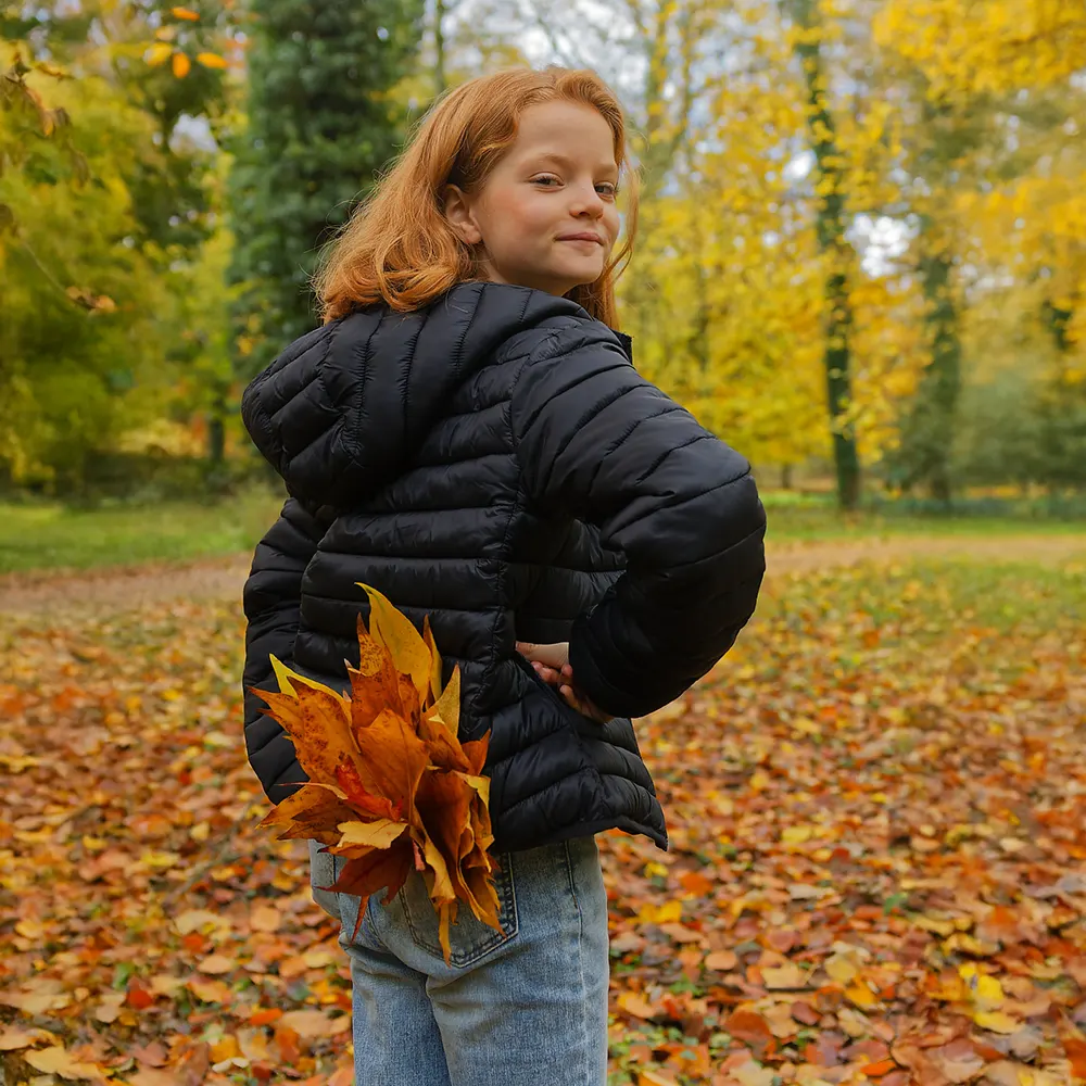 Portrait d'une jeune fille souriant de dos, tenant des feuilles d'automne dans sa poche.