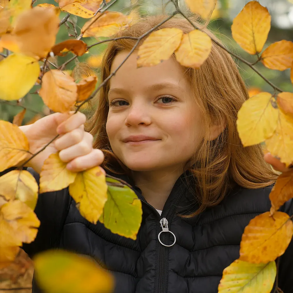 Portrait d'une jeune fille souriant dans un feuillage d'automne, pour une séance photo en extérieur.