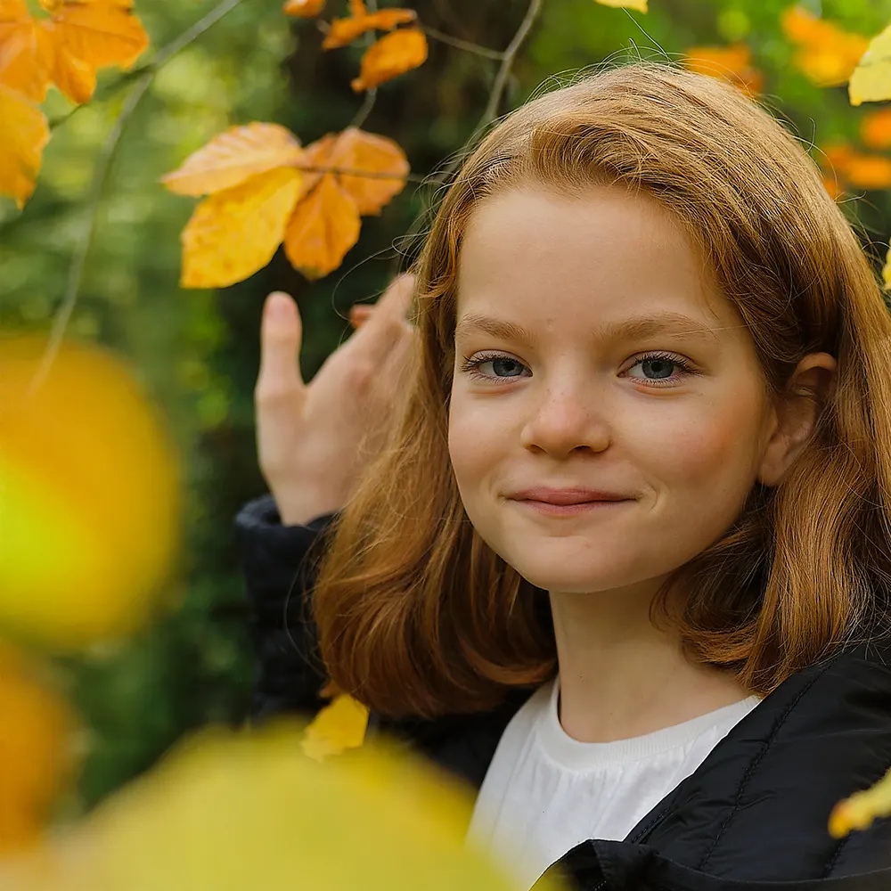 Portrait d'une jeune fille souriant dans un feuillage d'automne, pour une séance photo en extérieur.