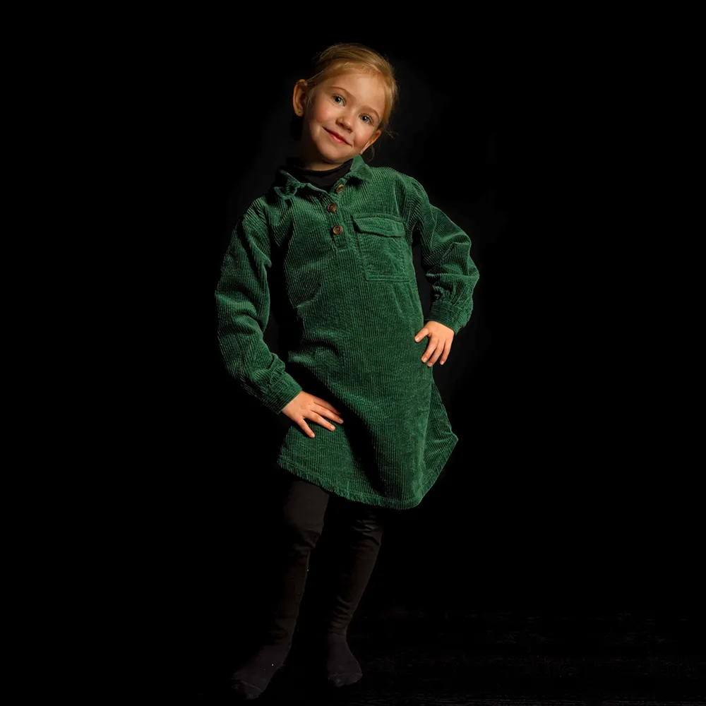 Portrait studio d'une petite fille en robe verte, posant sur un fond sombre.