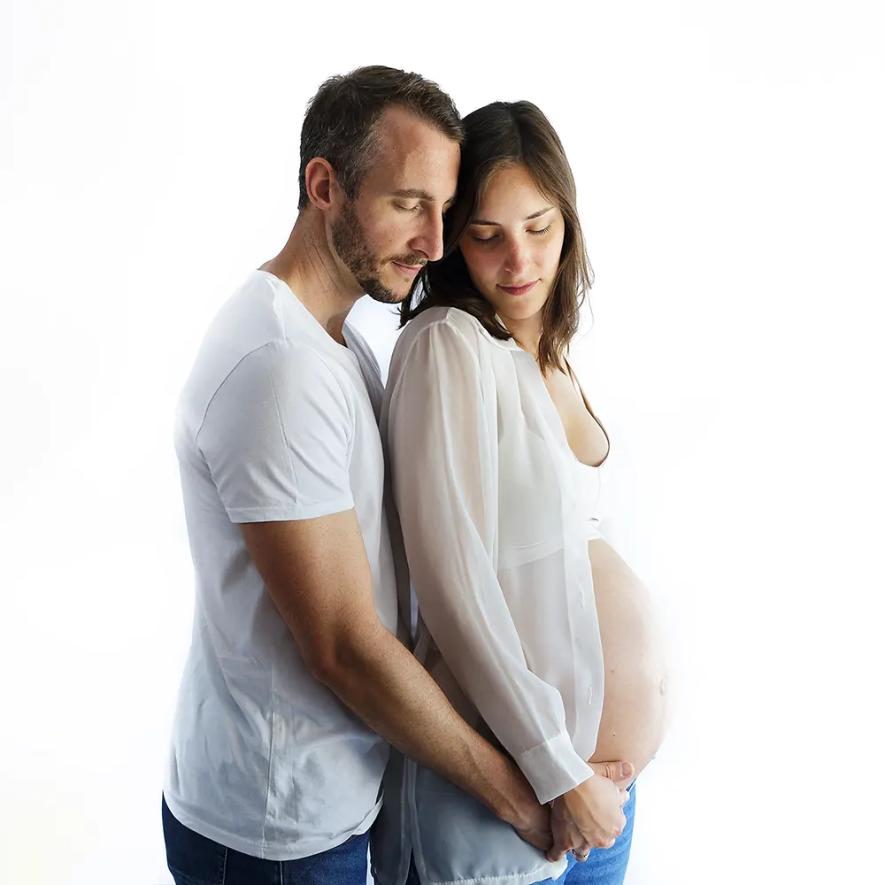 Portrait de grossesse en studio d'un couple se tenant tendrement. Le futur papa en t-shirt blanc et la future maman en brassière et jeans.