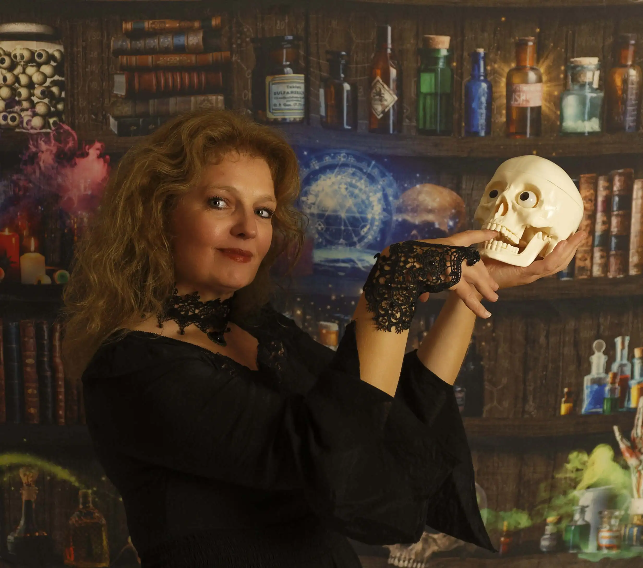 Femme devant une toile de fond tenu un crane dans ses mains. Ce fond de studio représente une étagère de sorcier, avec des livres, des potions, et autres accessoires.