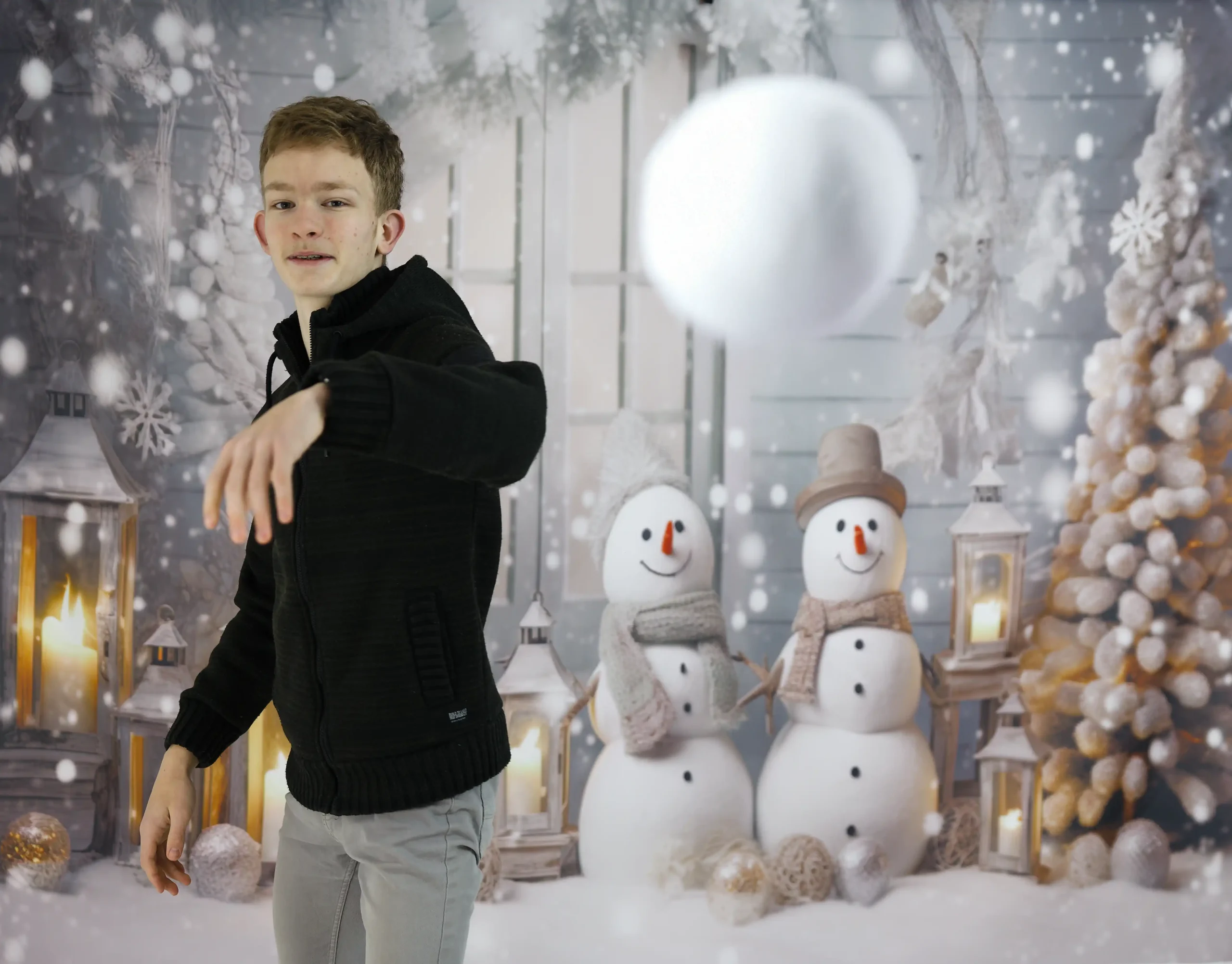 Adolescent devant un fond photo. Ce fond de studio représente un décor hivernal avec 2 bon homme de neige. Ce garçon lance une boule de neige.
