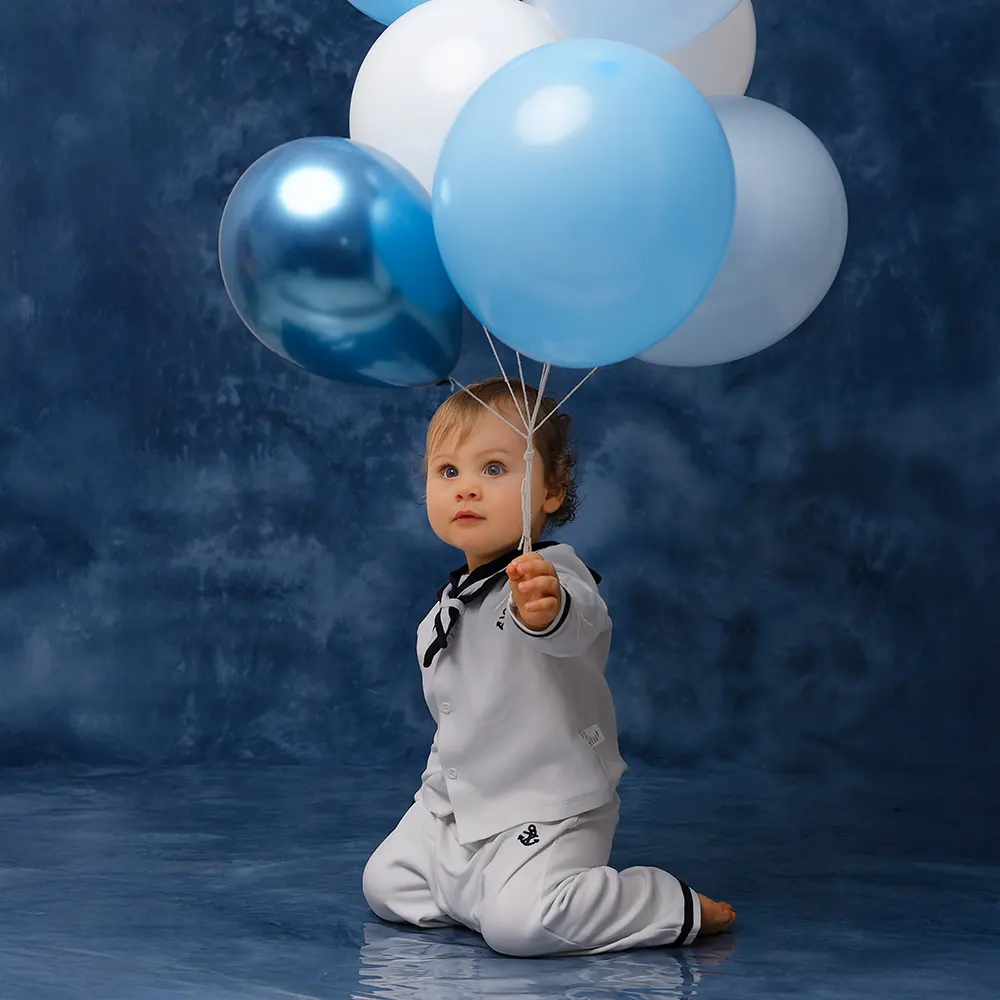 Séance photo d'anniversaire pour un bébé déguisé en matelot, tenant un bouquet de ballons bleus et blancs.