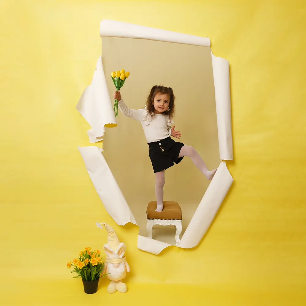 Séance photo d'une petite fille en studio, sortant d'une déchirure de papier, avec un bouquet de tulipes jaunes à la main.